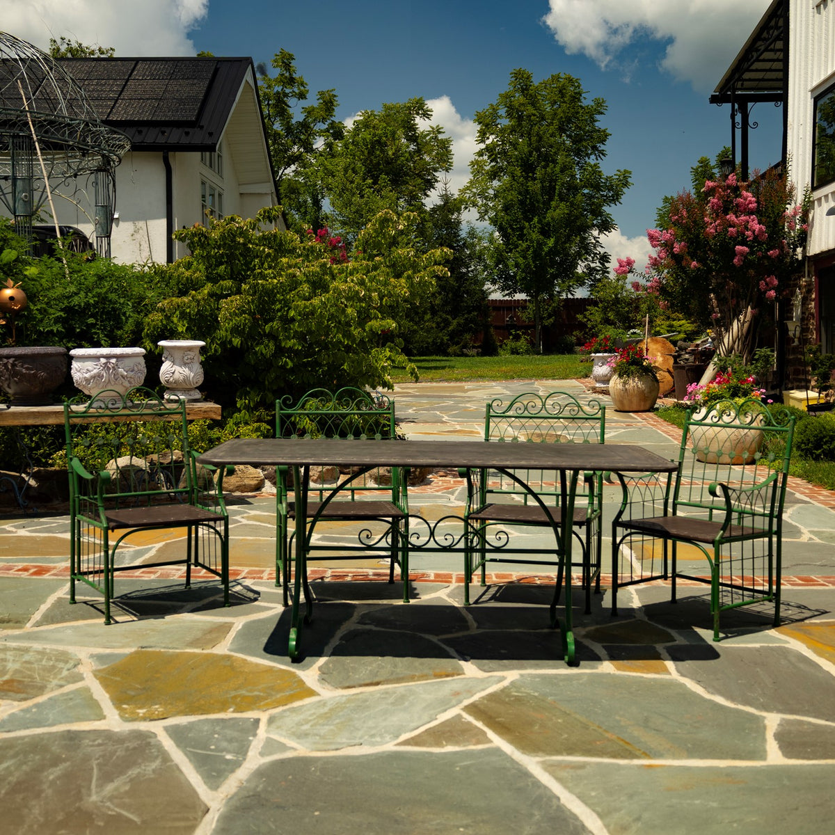 Green metal dining table and chairs with brown seats on a stone patio among garden plants.