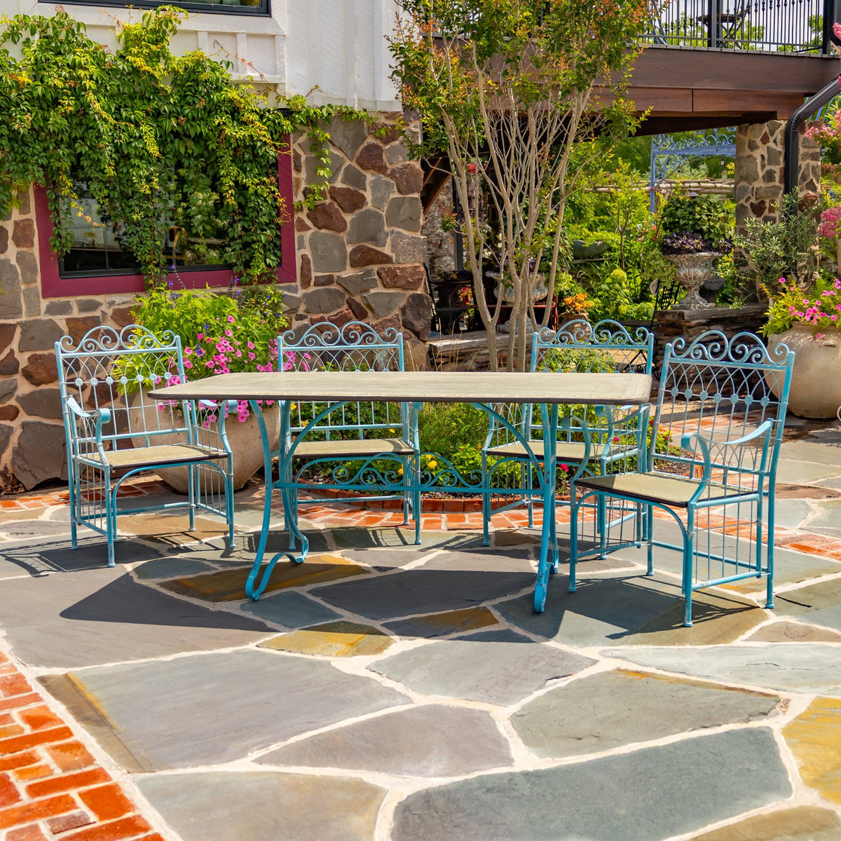 Blue metal dining set with a rectangular table and decorative chairs on a stone patio.