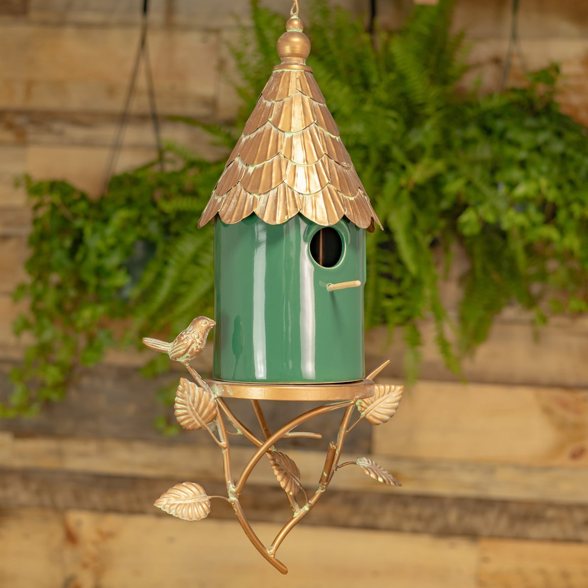 Hanging green birdhouse with a scalloped copper-tone roof, decorative metal stand, and small bird ornaments.