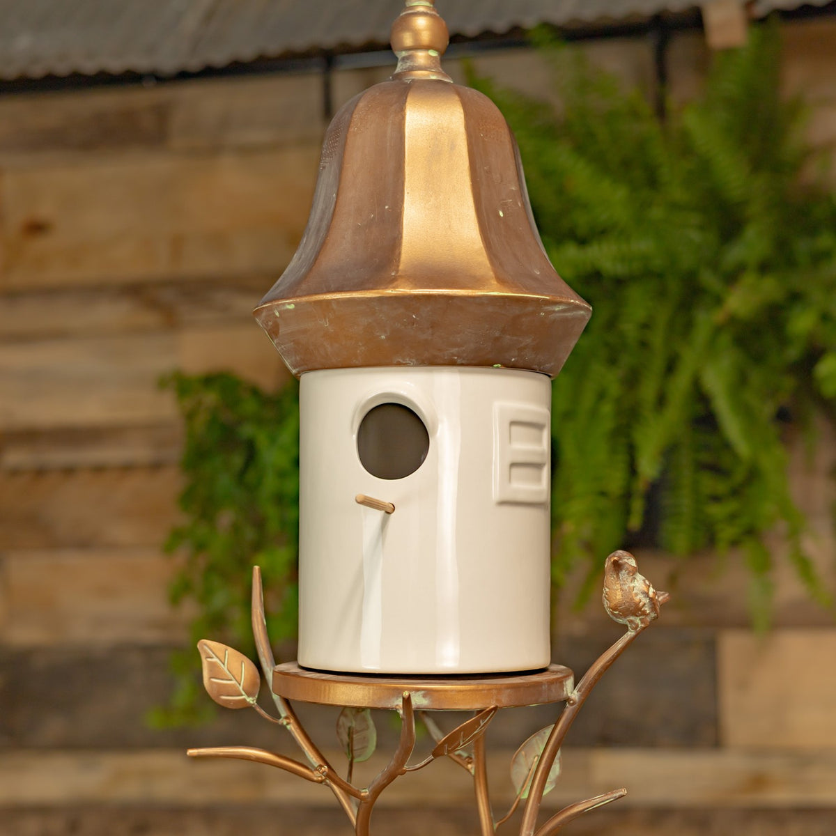 White cylindrical birdhouse with a copper-tone roof and leafy metal hanger, shown close up.