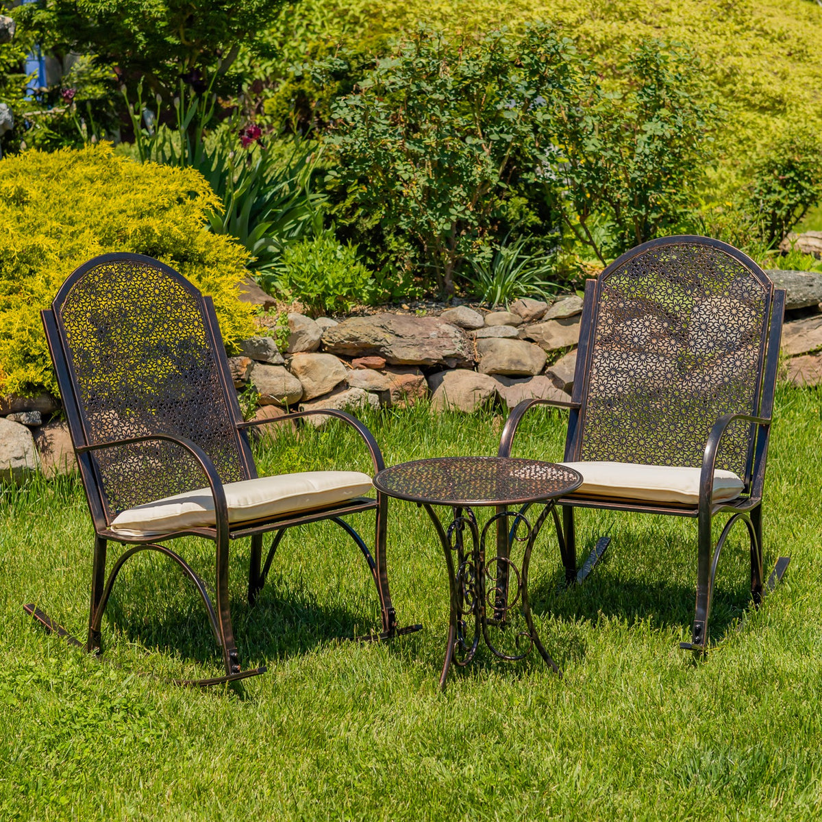 Two dark metal rocking chairs with cream cushions flank a round patterned garden table on a lawn.