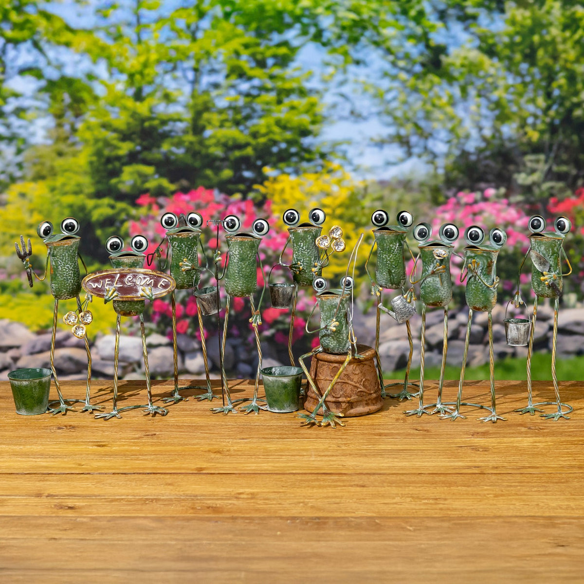 A row of whimsical metal frogs, some holding small garden tools or flowers, displayed on a wooden bench.