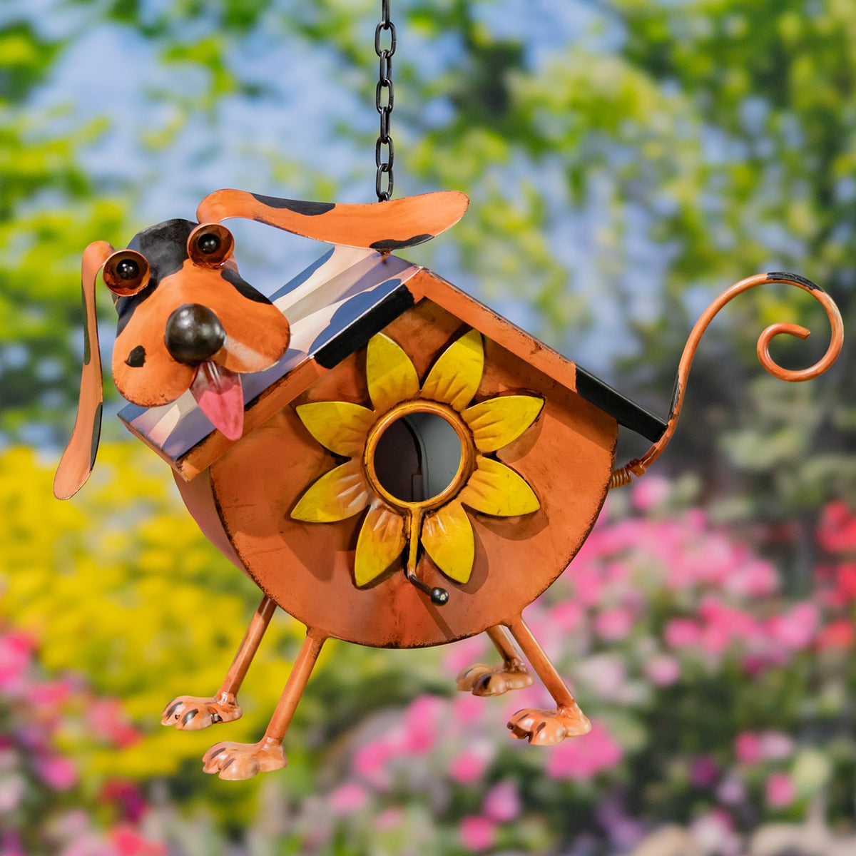 Orange dog-shaped metal birdhouse with a sunflower entrance, hanging against a garden backdrop.