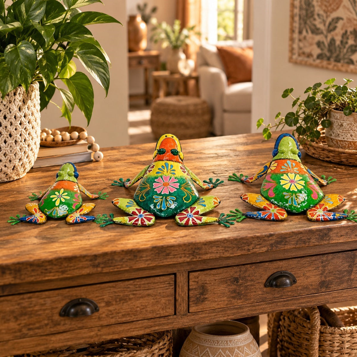 Three brightly painted frog statues sit on a wooden console table among plants and woven decor.