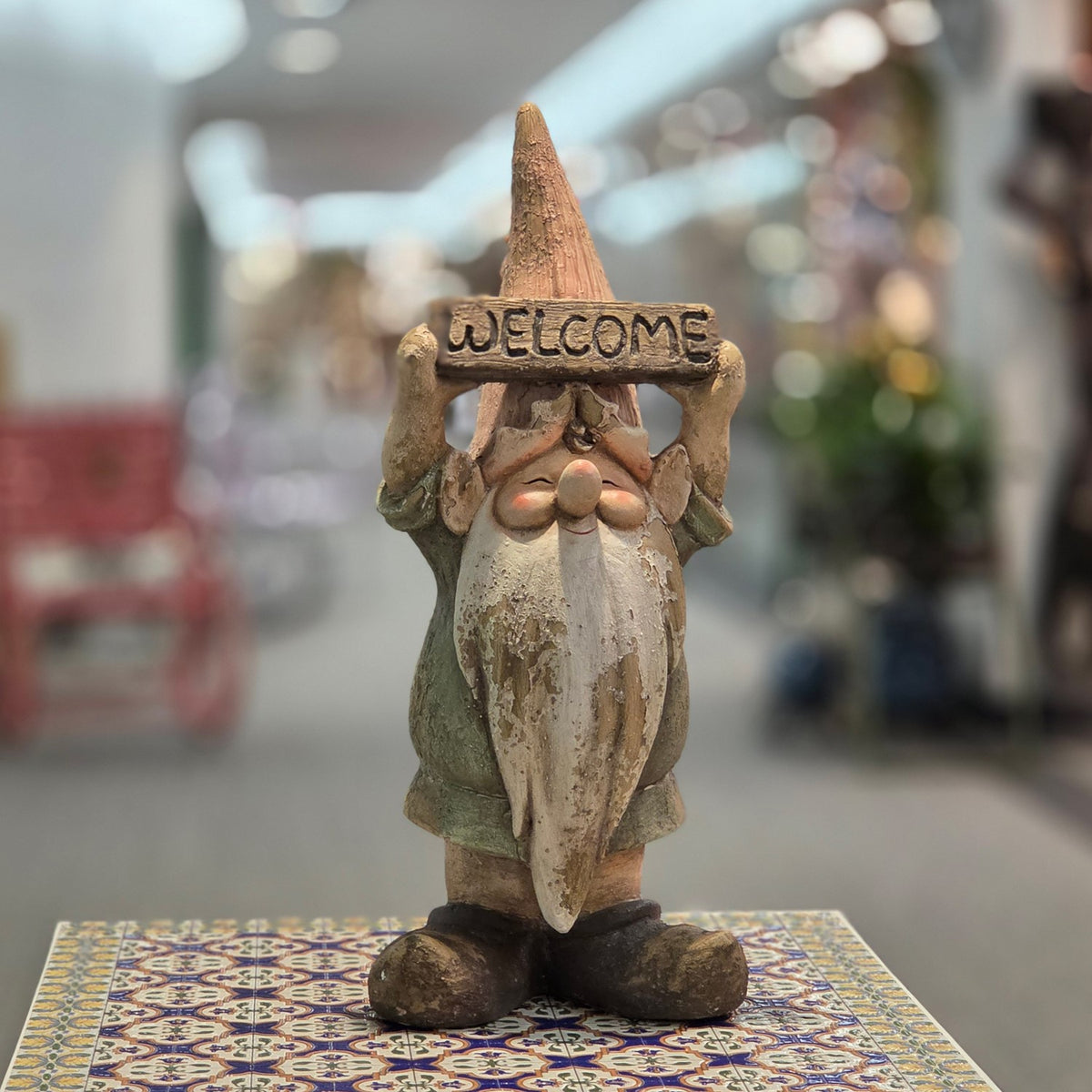 Front view of a rustic garden gnome holding a welcome sign on a patterned table