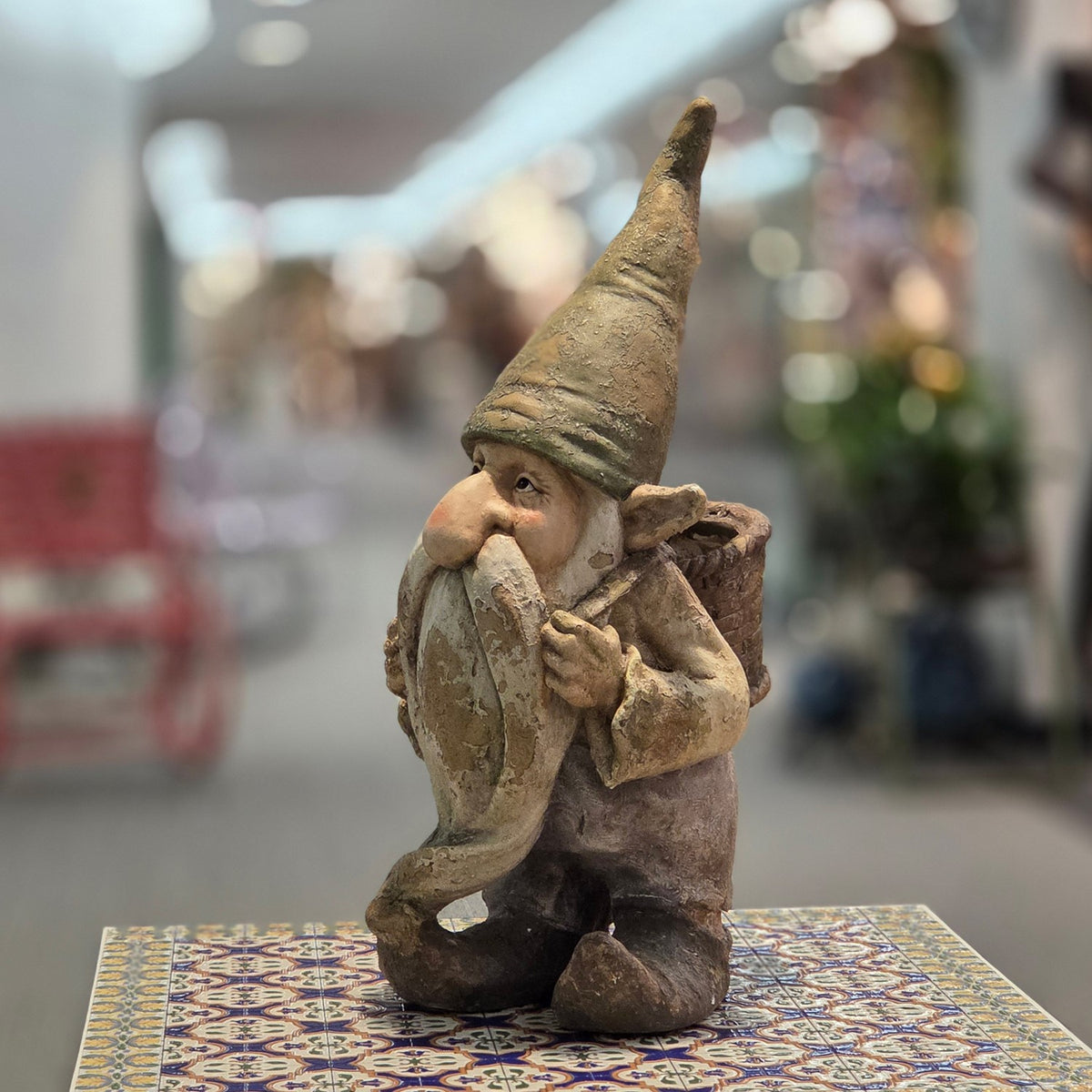 Distressed garden gnome with a back basket planter, shown from the front on a patterned table