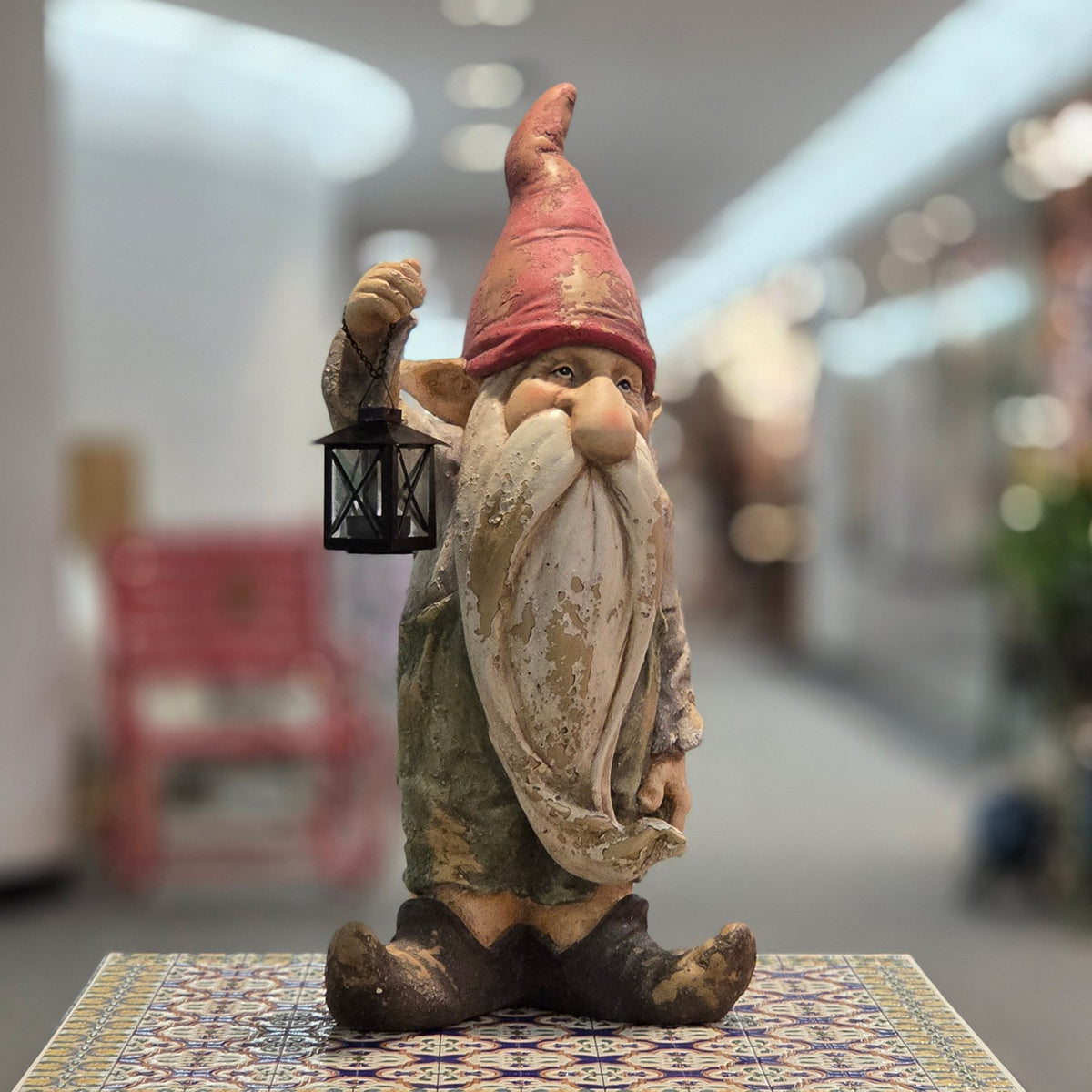 Front view of a distressed garden gnome with red hat and black lantern