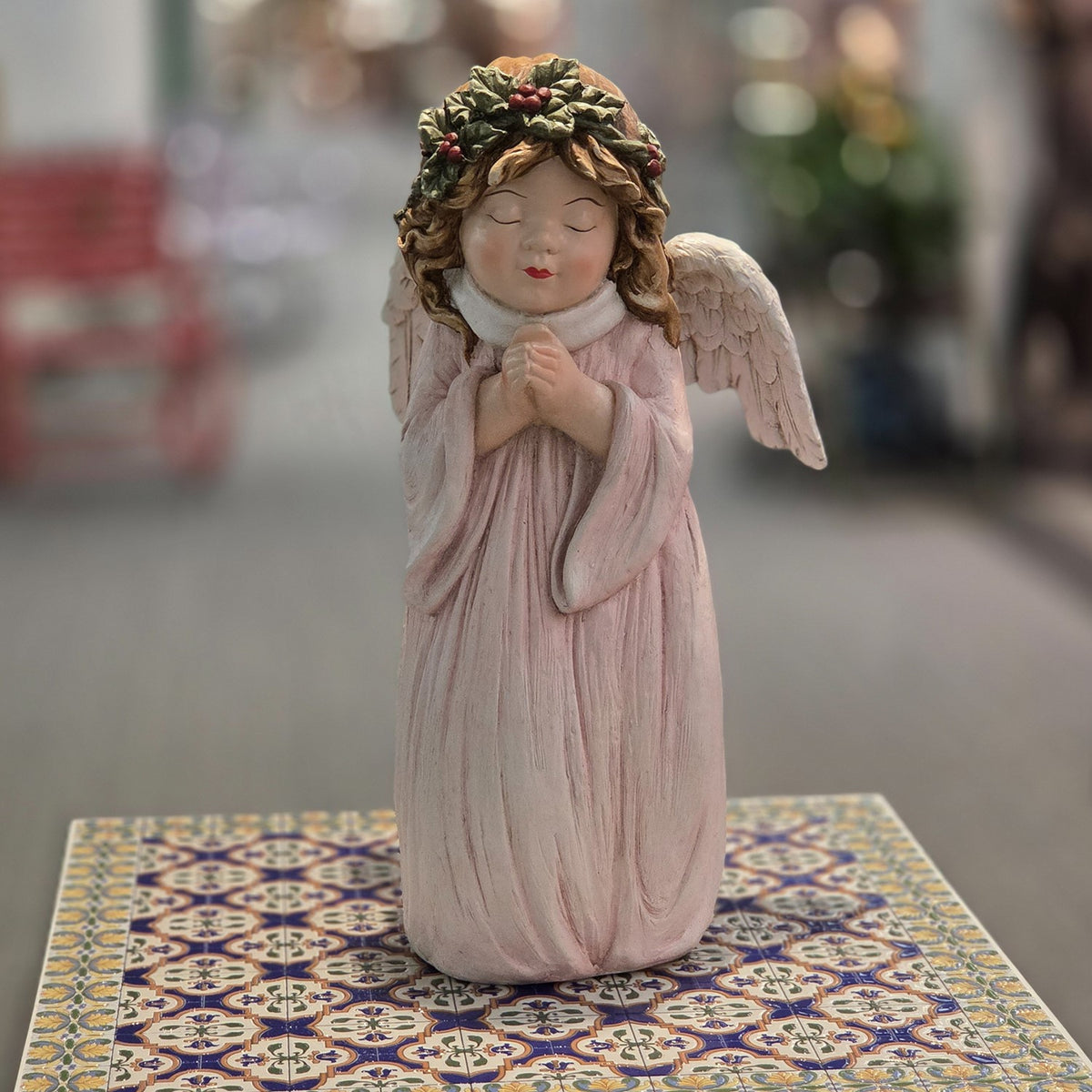 Front view of a praying angel in a blush gown with white wings and holly crown