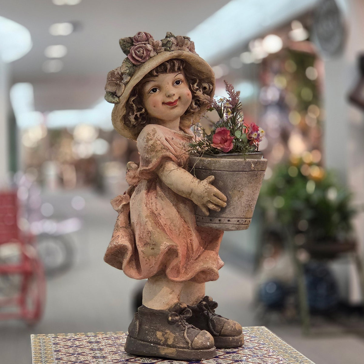 Pastel girl figurine holding a flowerpot with flowers, front three-quarter view