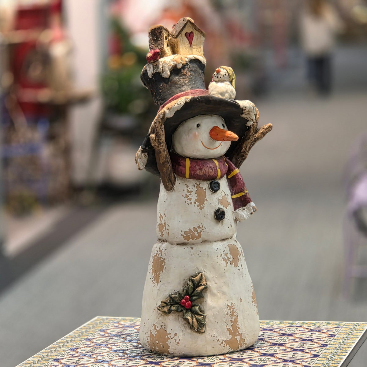 Full snowman figurine with tall hat, facing forward on a patterned table
