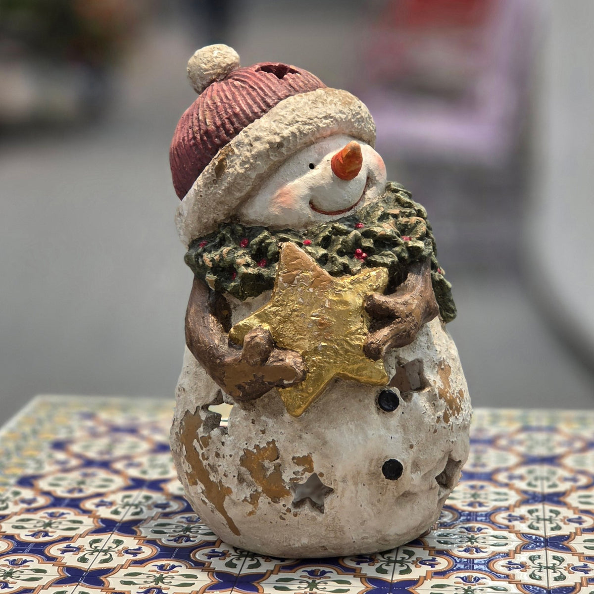 Distressed snowman candleholder with gold star, viewed from the front on a patterned table
