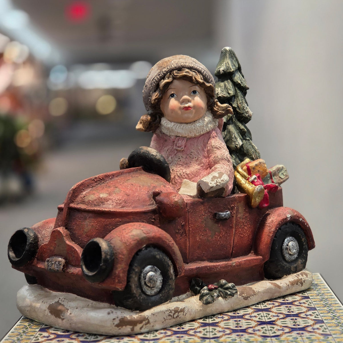 Front three-quarter view of a girl in a weathered red truck with a tree and gifts