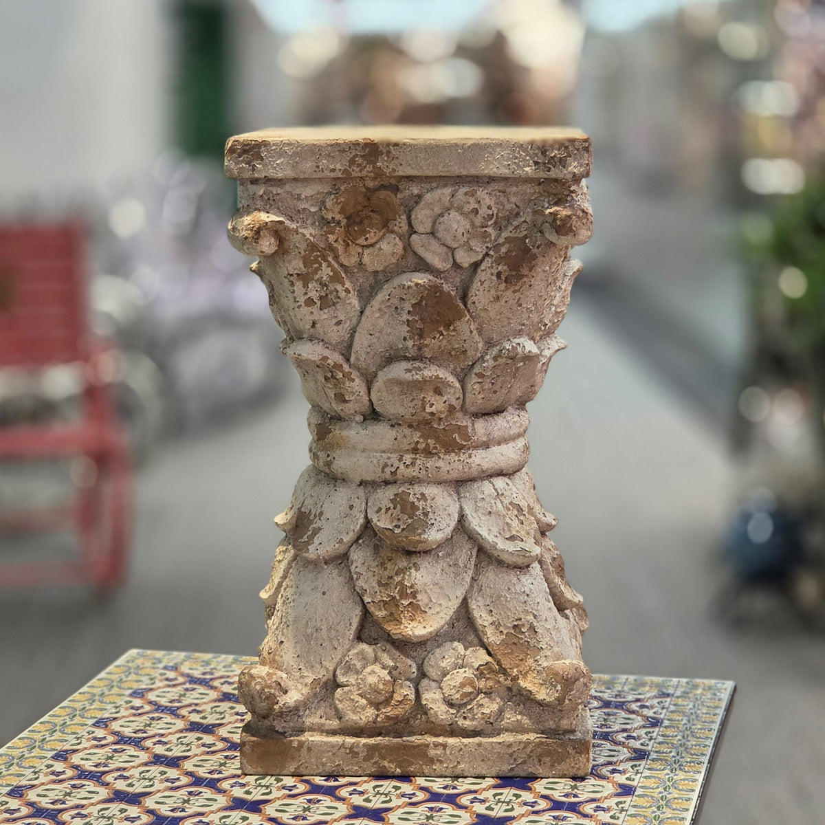 Distressed grey-brown carved pedestal stand shown upright on a patterned tabletop