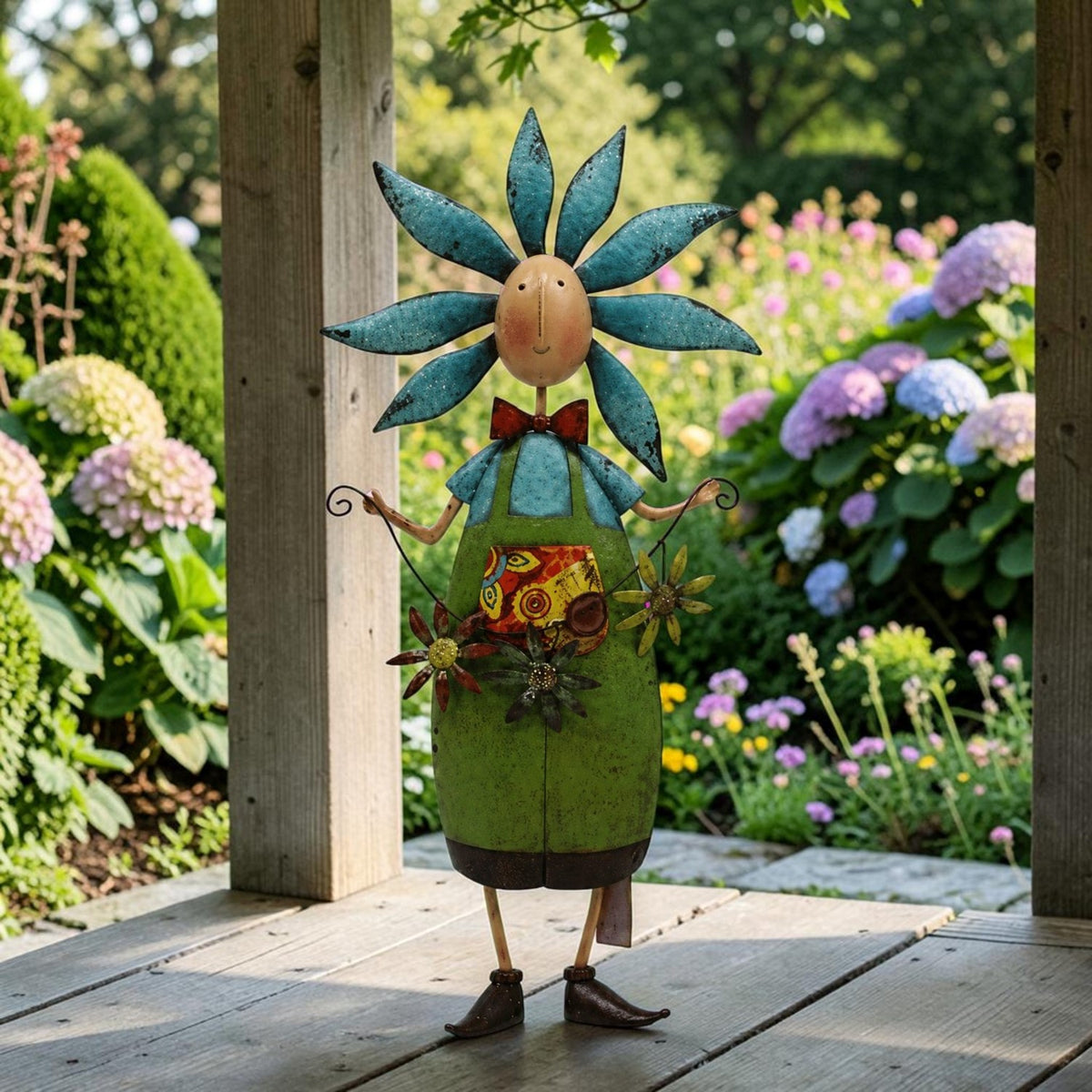 Colorful metal flower figure stands on a wooden porch amid blooming garden flowers.
