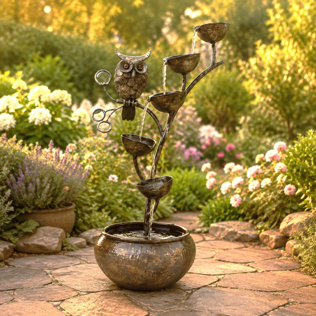 Owl-and-branch fountain with cascading bowls in a flower garden patio setting.