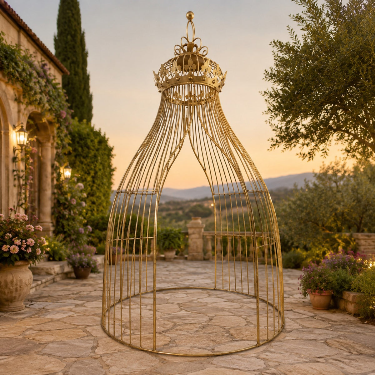 Tall gilded metal pavilion with a crown-shaped top on a stone patio surrounded by flowers and greenery.