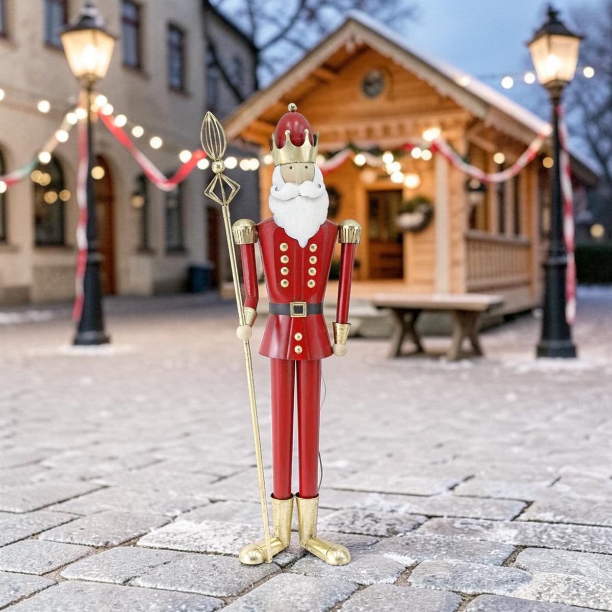 Red-and-gold king figurine holding a tall gold staff in a decorated outdoor holiday setting.