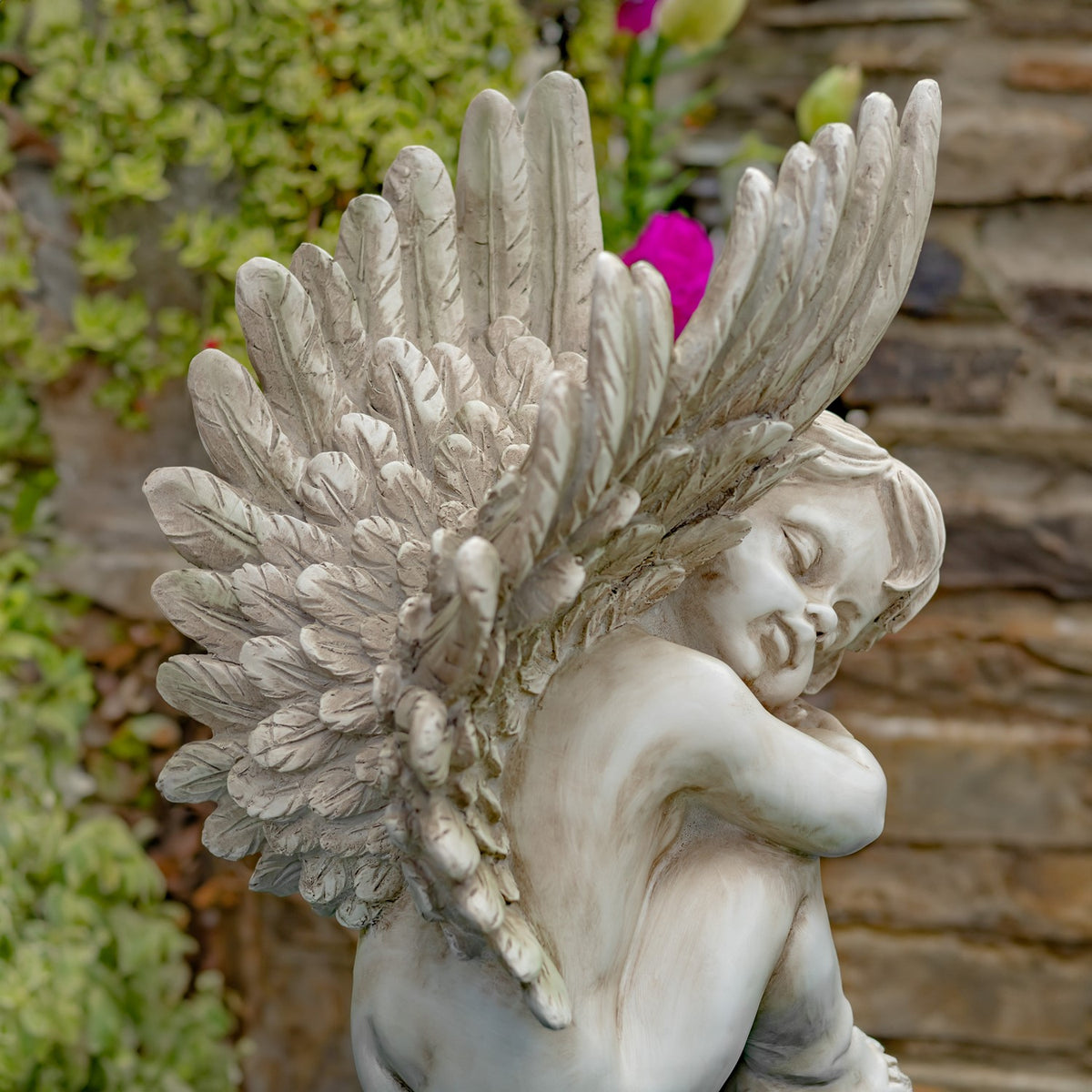 Close view of an antique grey cherub statue and its detailed wings