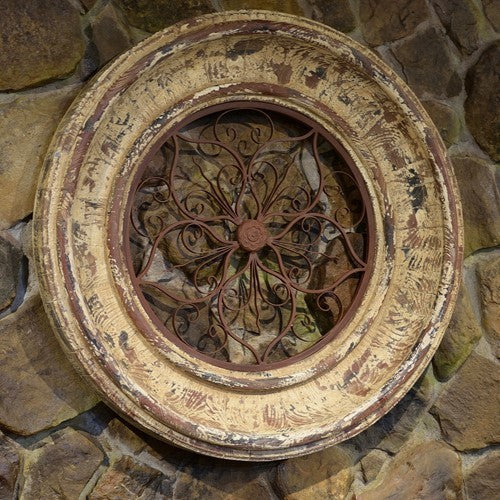 Round distressed wooden frame with iron center displayed against a stone wall