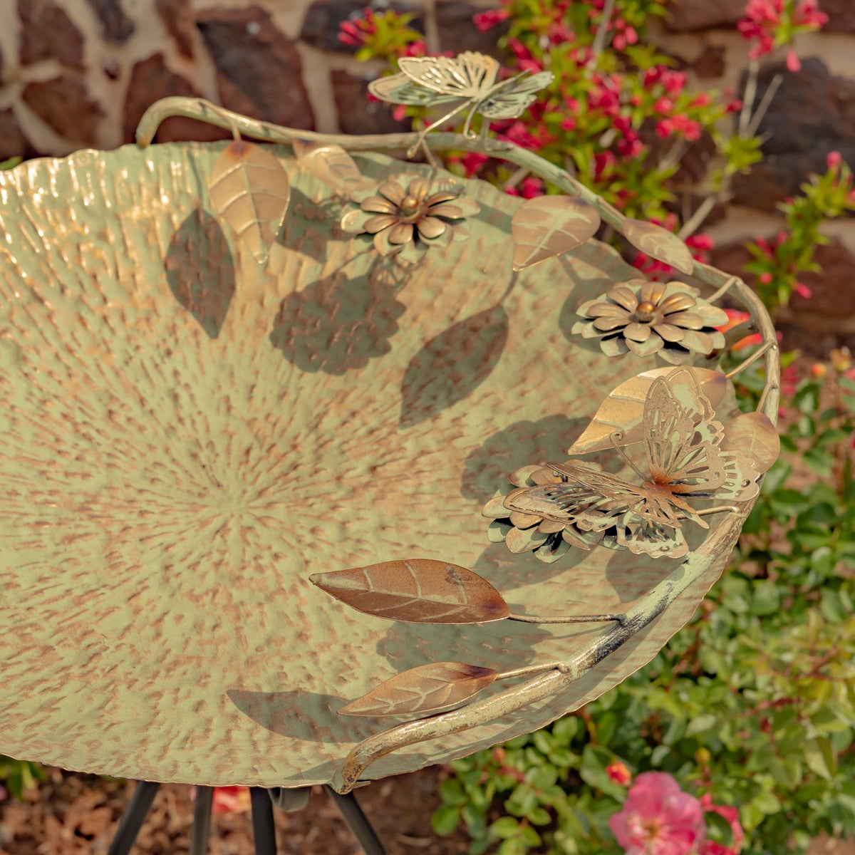 Close-up of a frosted gold birdbath bowl with raised butterfly and flower details.