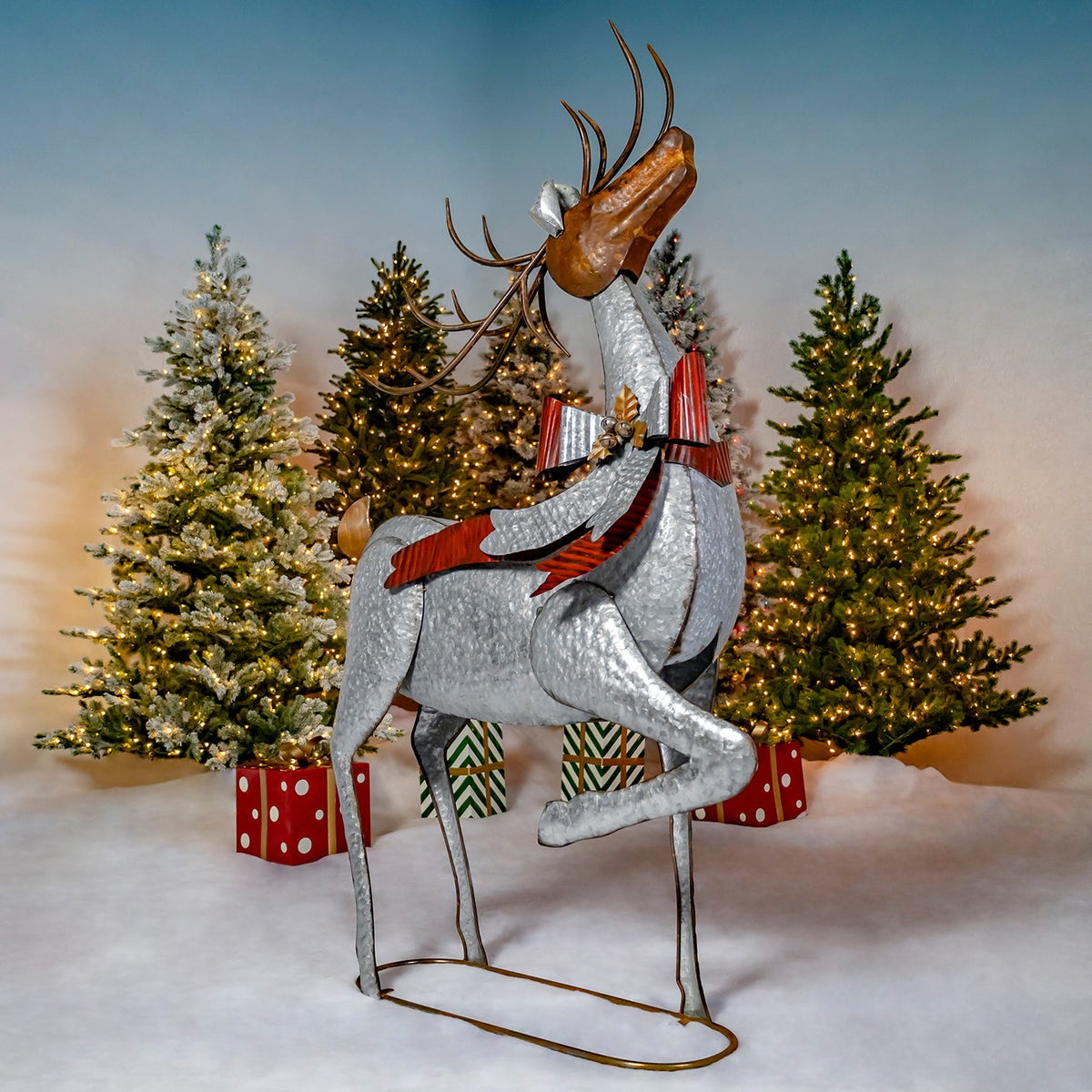 A standing silver reindeer with raised front leg and striped bow stands among decorated holiday trees.