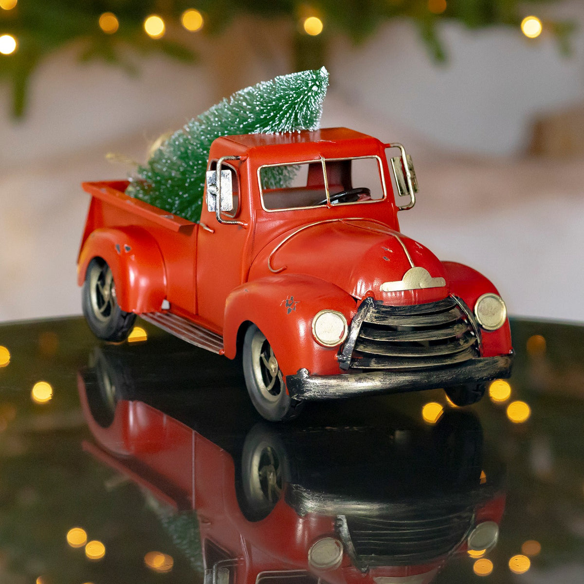 Red vintage pickup with a miniature evergreen in its bed, viewed from the front and driver side.