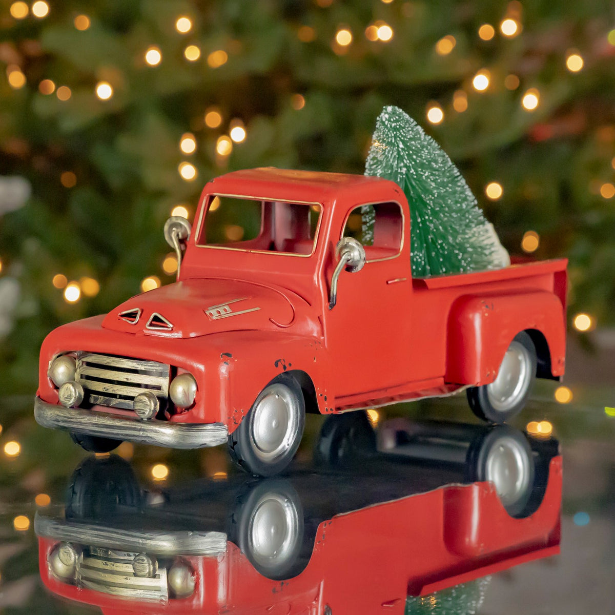 Red vintage-style pickup with a bottle-brush tree in its bed, viewed from the front.