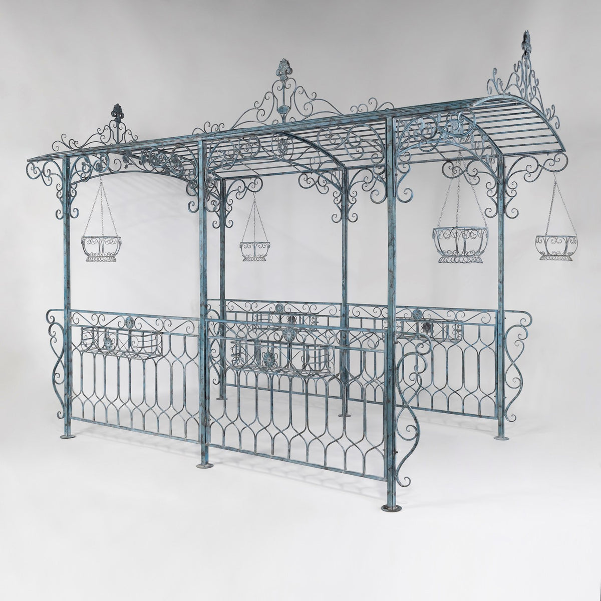 Dark blue ornate iron gazebo with hanging baskets shown against a plain studio background