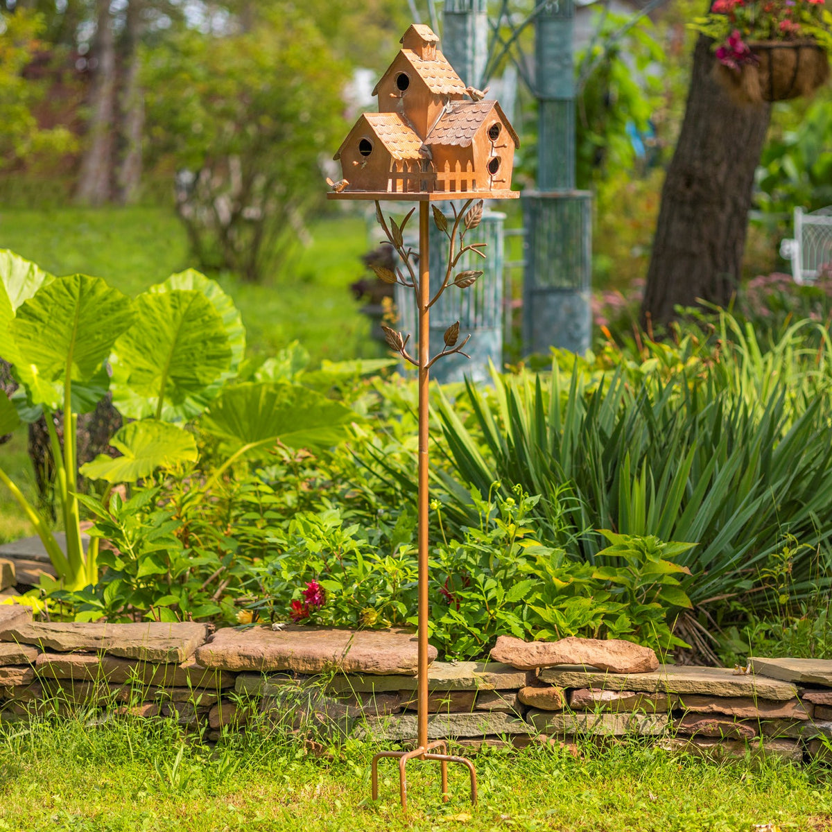 Full birdhouse stake with four-prong base standing in a lush garden