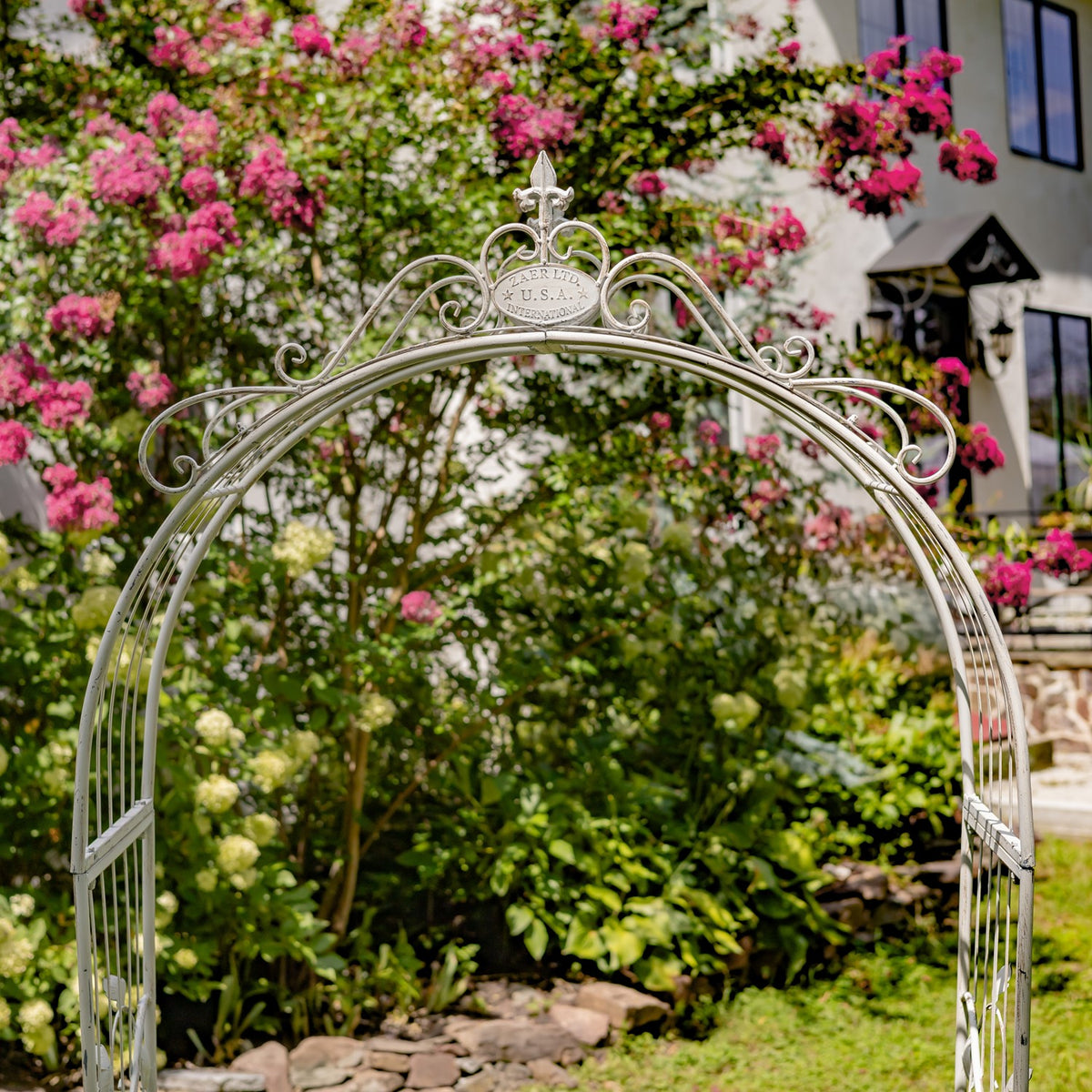 Close view of the ornate arch top and scrollwork against flowering shrubs