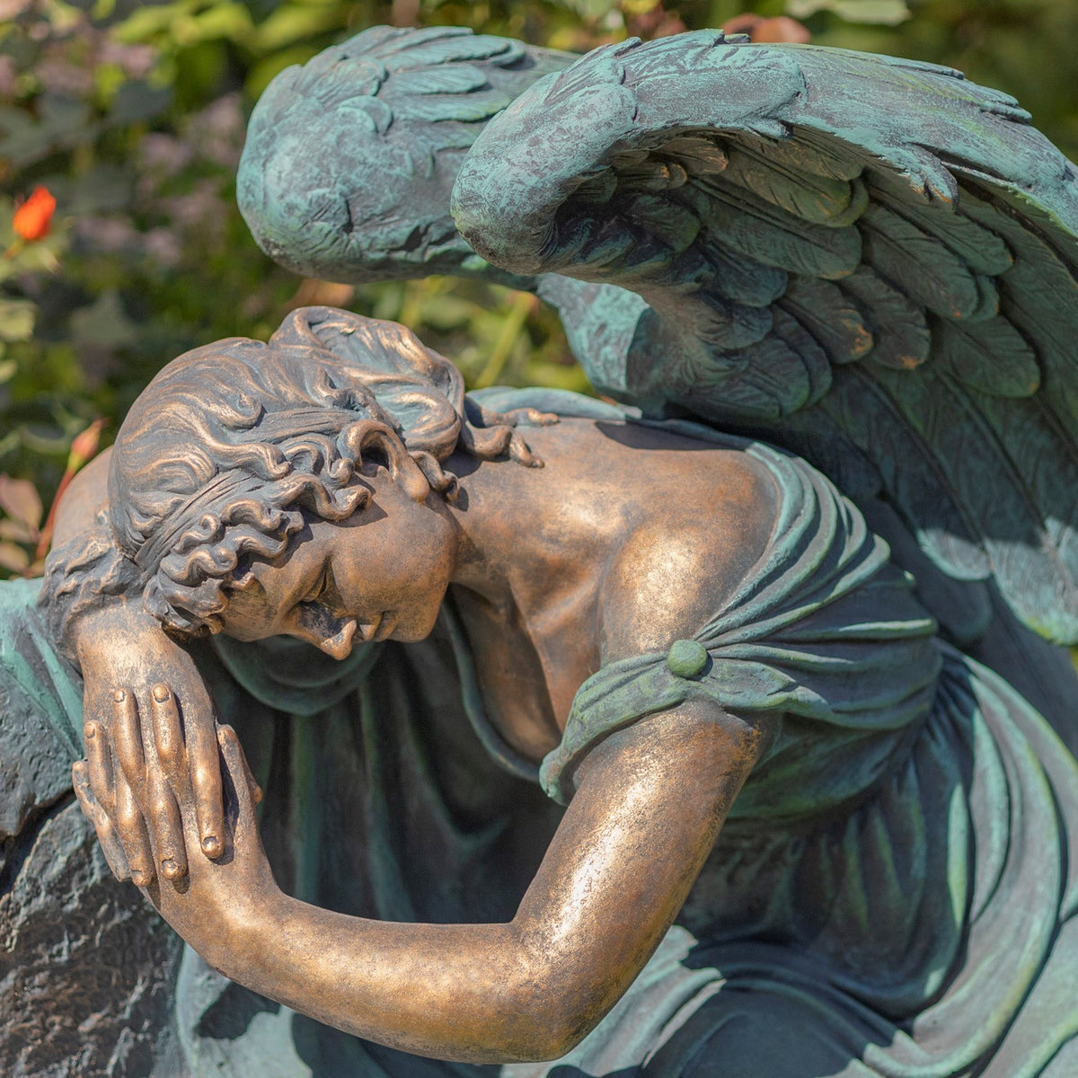 Close view of the angel's bowed face, clasped hands, draped robe, and layered wing feathers.