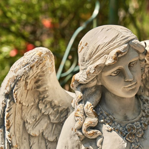 Close-up of the angel’s face, curled hair, wing and decorative neckline in a pale weathered finish.