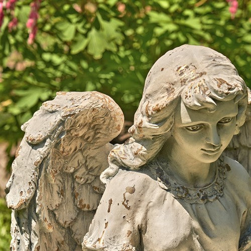 Close view of the angel’s face, curled hair, wing, and weathered robe.