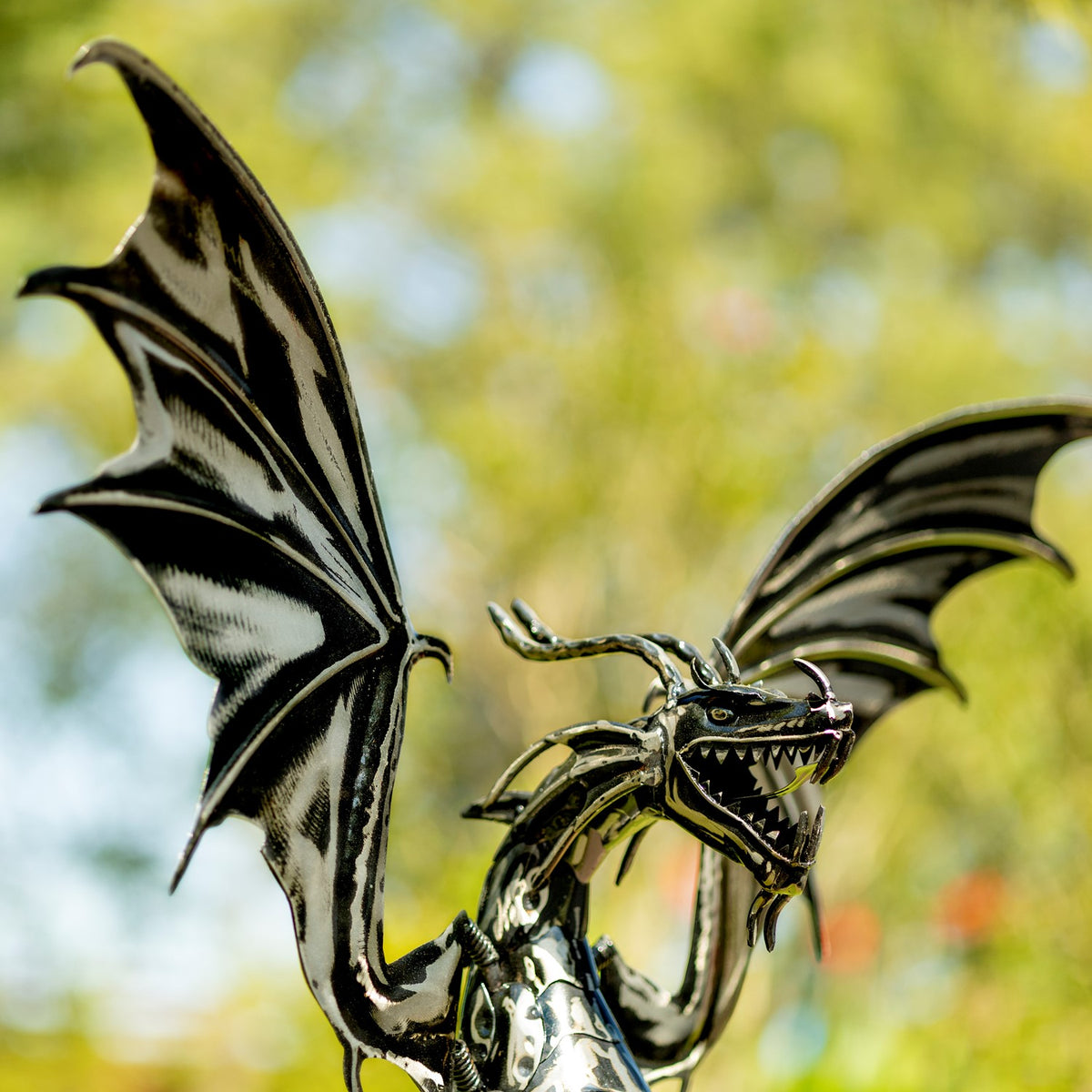 Close angled view of the metal dragon's raised wings, curved horns, and open toothed mouth.