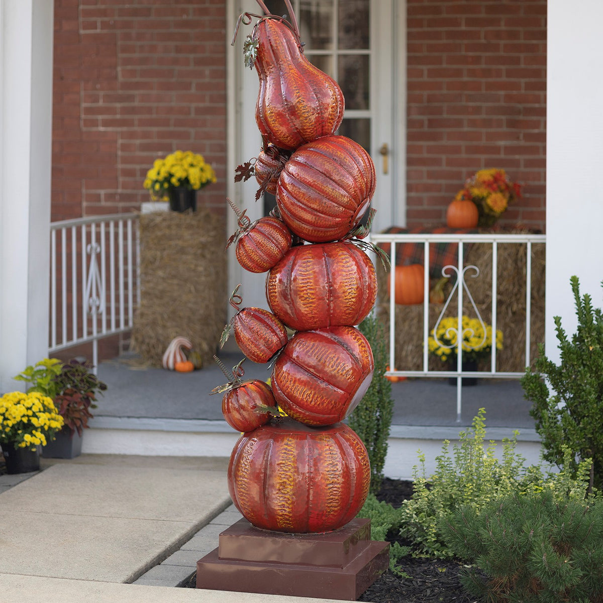 Close view of a stacked orange pumpkin column on a square base beside a garden path.