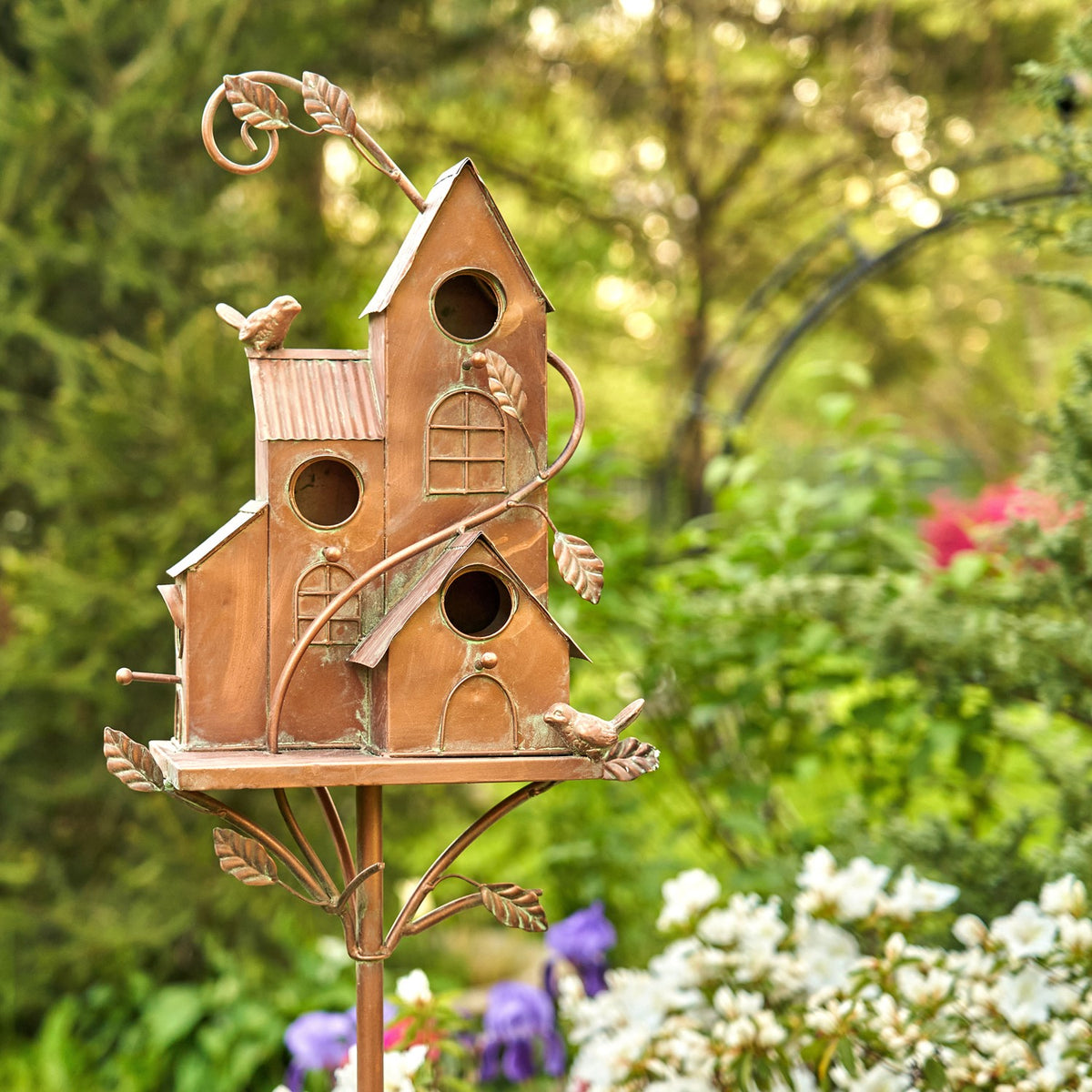 Antique copper iron birdhouse stake shown upright among garden flowers