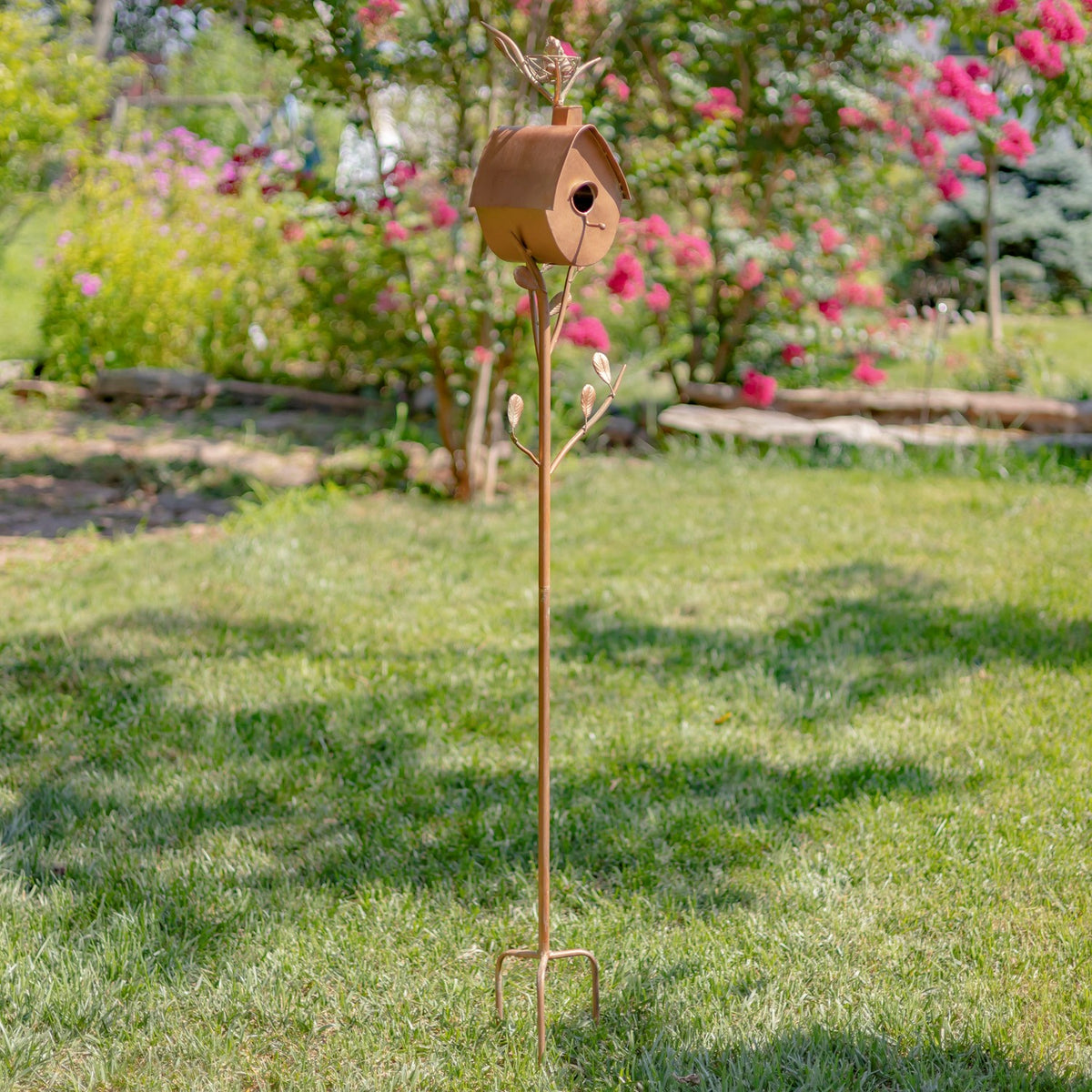 Full view of a tall birdhouse stake standing in a lawn, with a small house above a forked ground point.