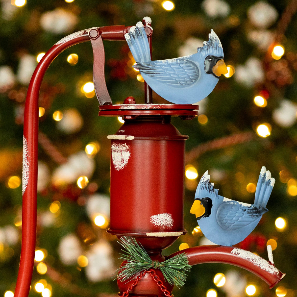 Close-up of two blue bird ornaments perched on the pump, showing its distressed red finish and curved handle.