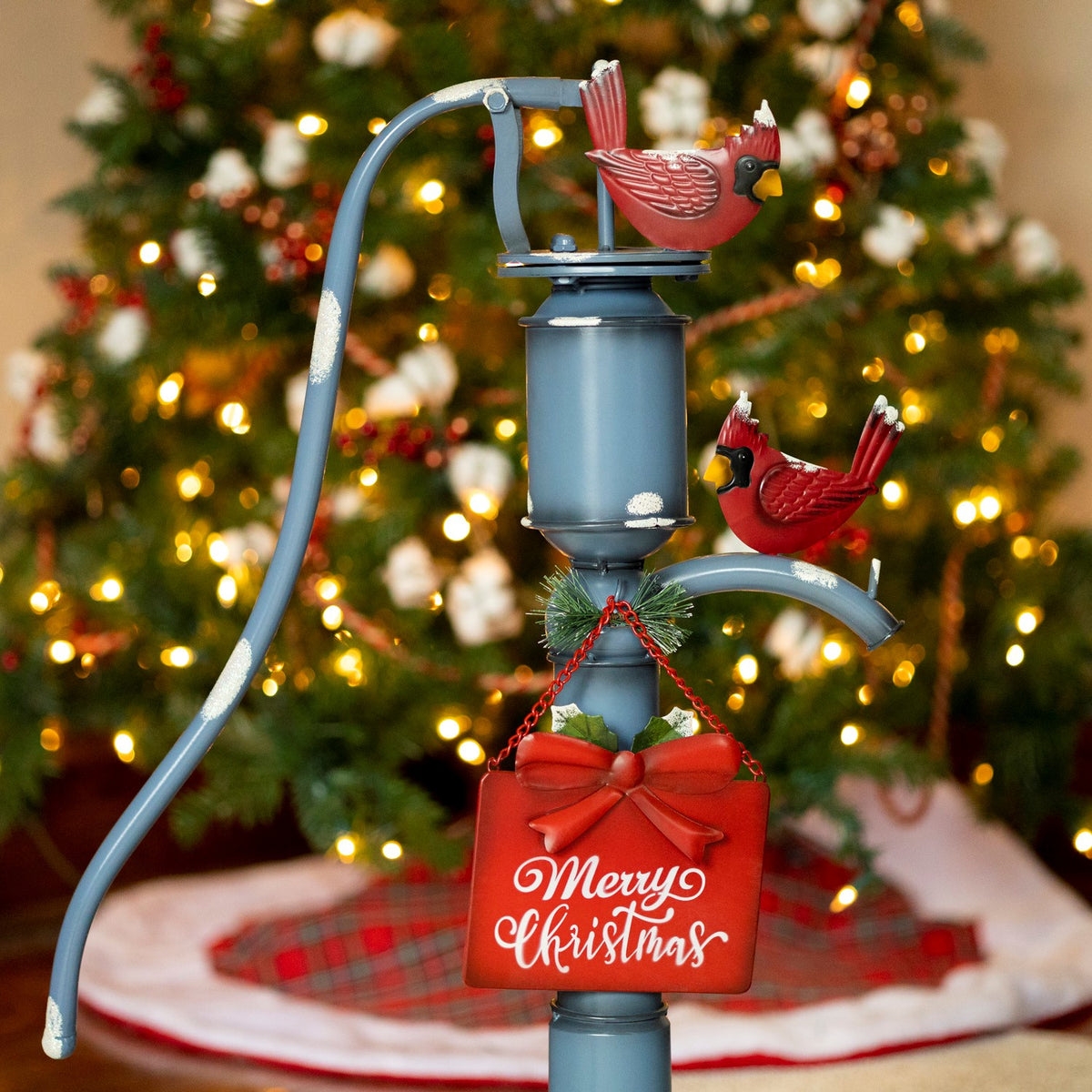 Closer view of the blue pump, red cardinal figures, greenery, and a red holiday sign against the tree.
