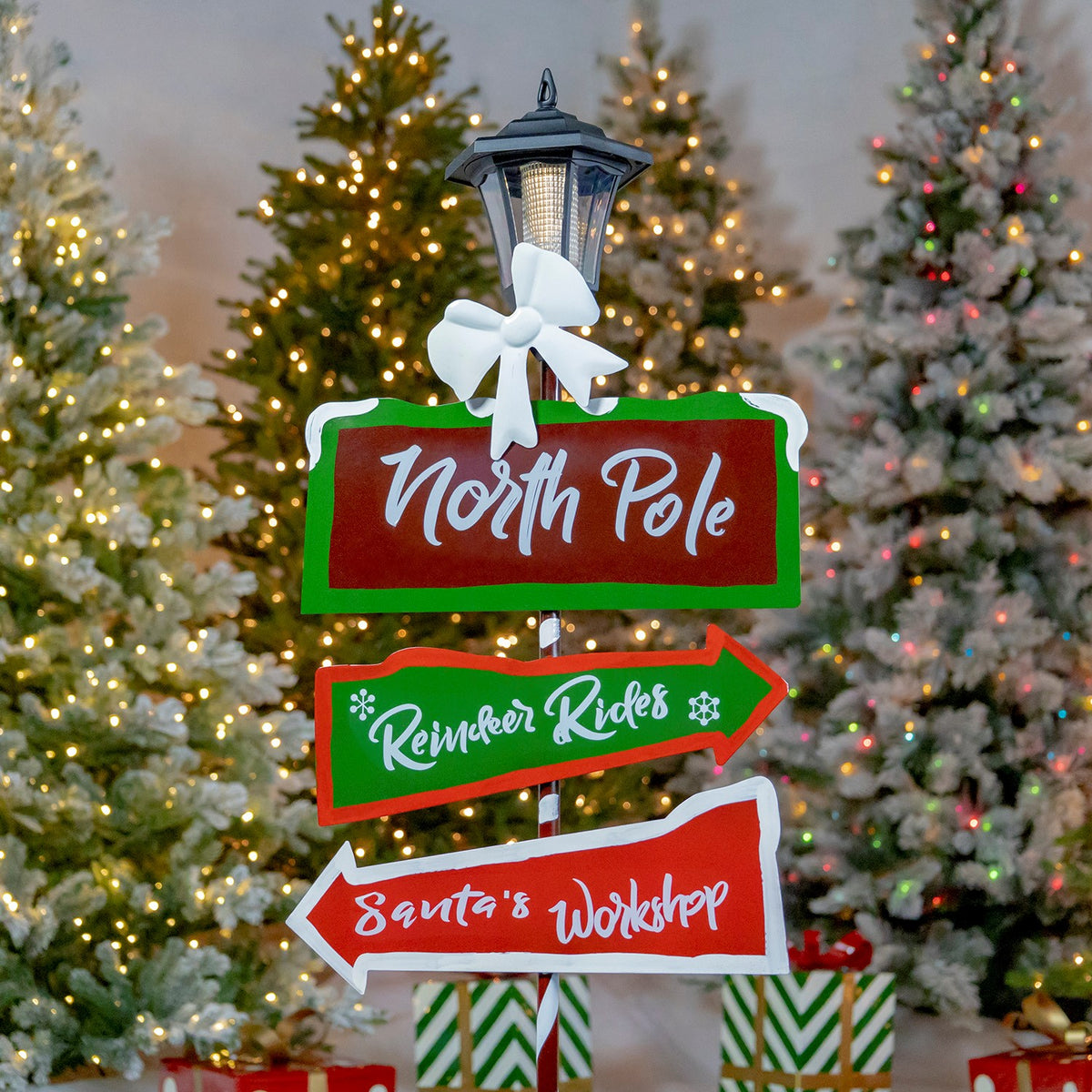 The holiday signpost fills the frame, showing its lantern, white bow, three colorful directional signs, and snowy tree