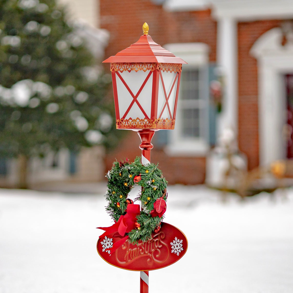Closer view of the red lantern, decorated wreath, bow, and holiday plaque against a snowy yard.