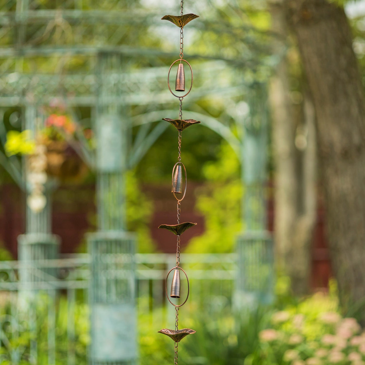 A longer section of the rain chain hangs vertically outdoors, alternating mushroom-shaped cups and oval-framed chimes.