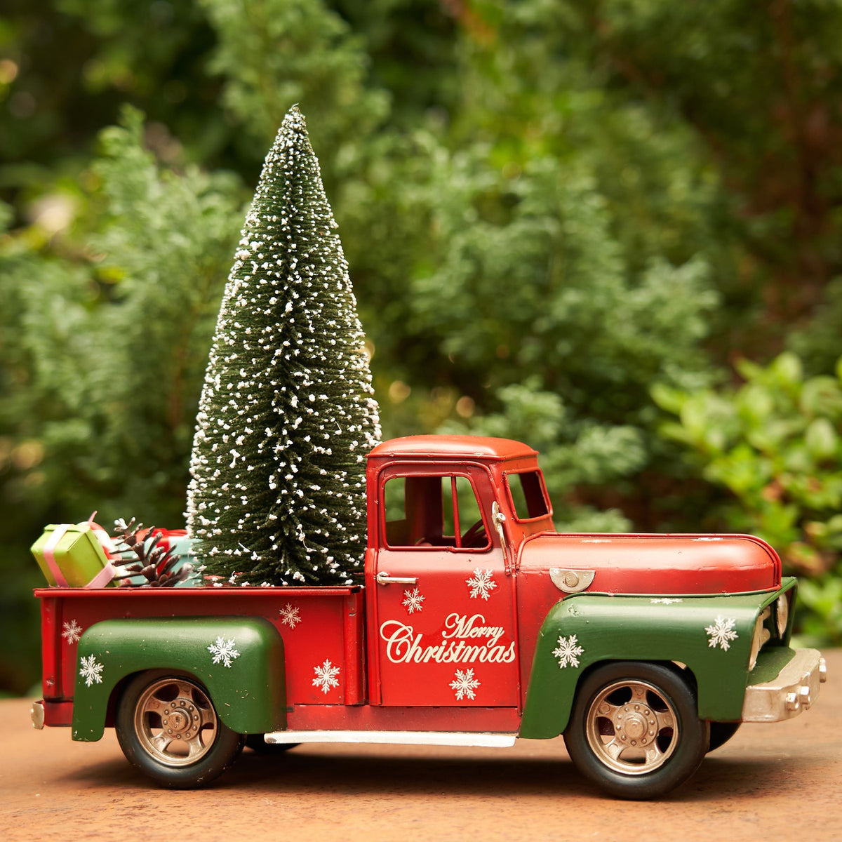 Side view of a red and green snowflake-decorated Christmas truck with a miniature tree