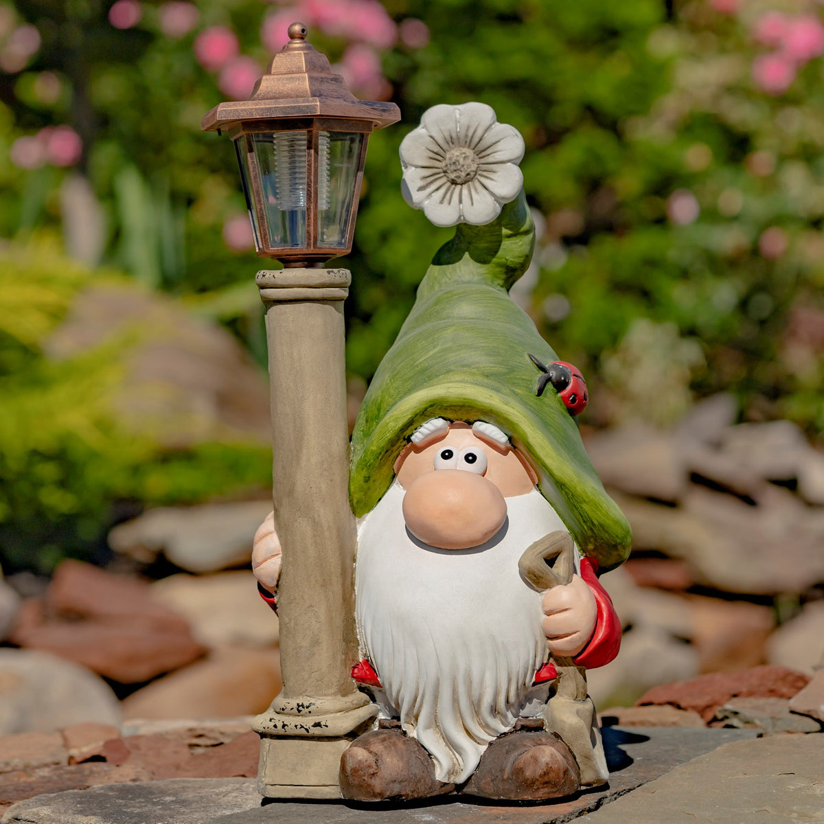 Close view of a green-hatted gnome beside its solar lantern on a stone path
