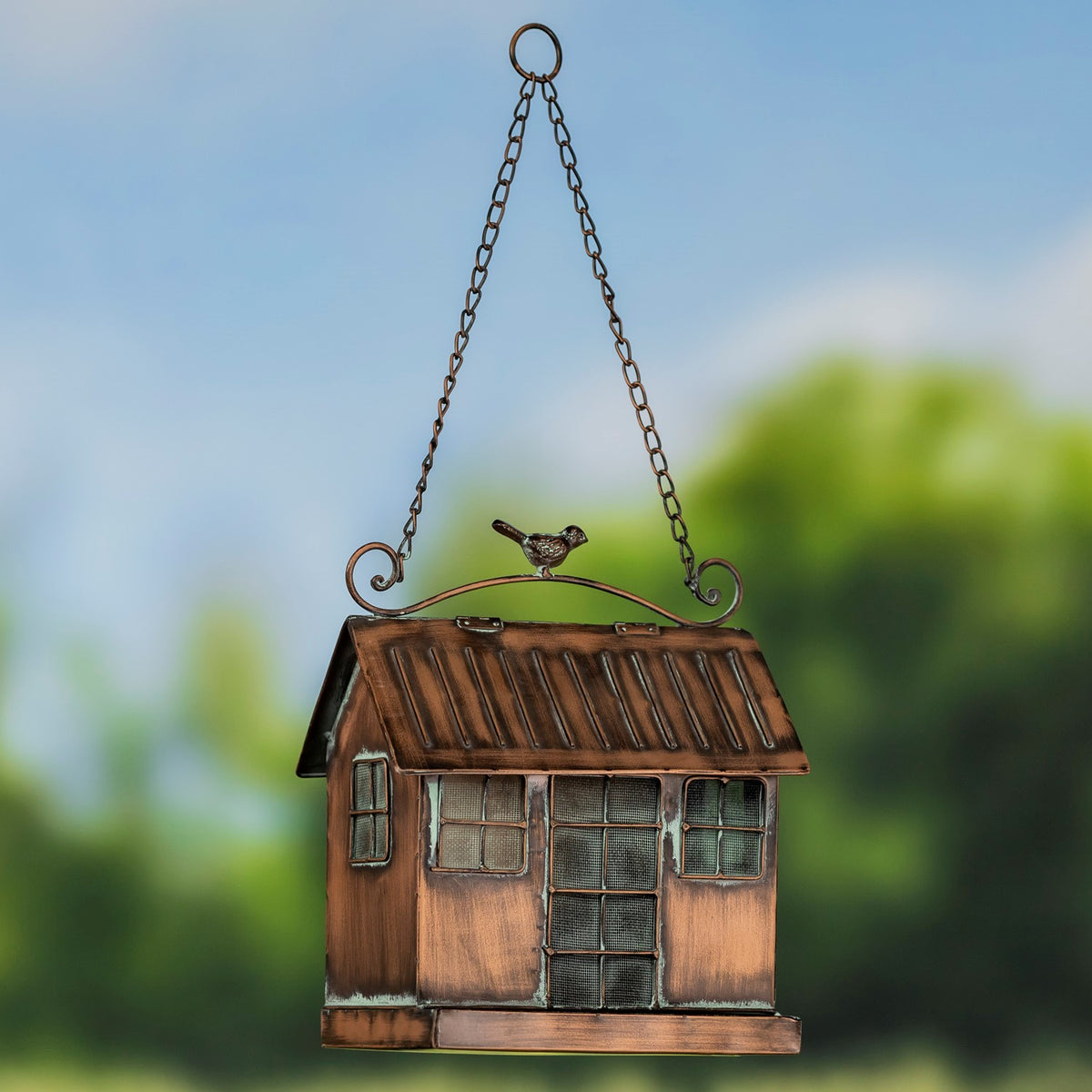 The house-shaped feeder hangs from two chains, showing its front openings, sloped roof, and lower tray.