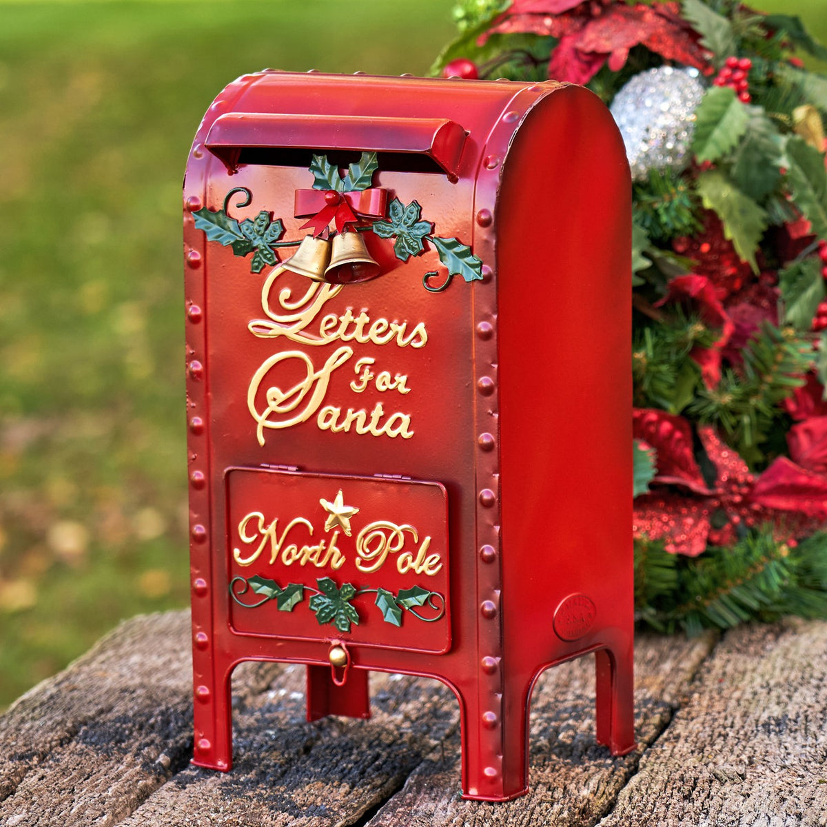Angled view of a red holiday mailbox with a curved top, front slot, and decorative greenery.