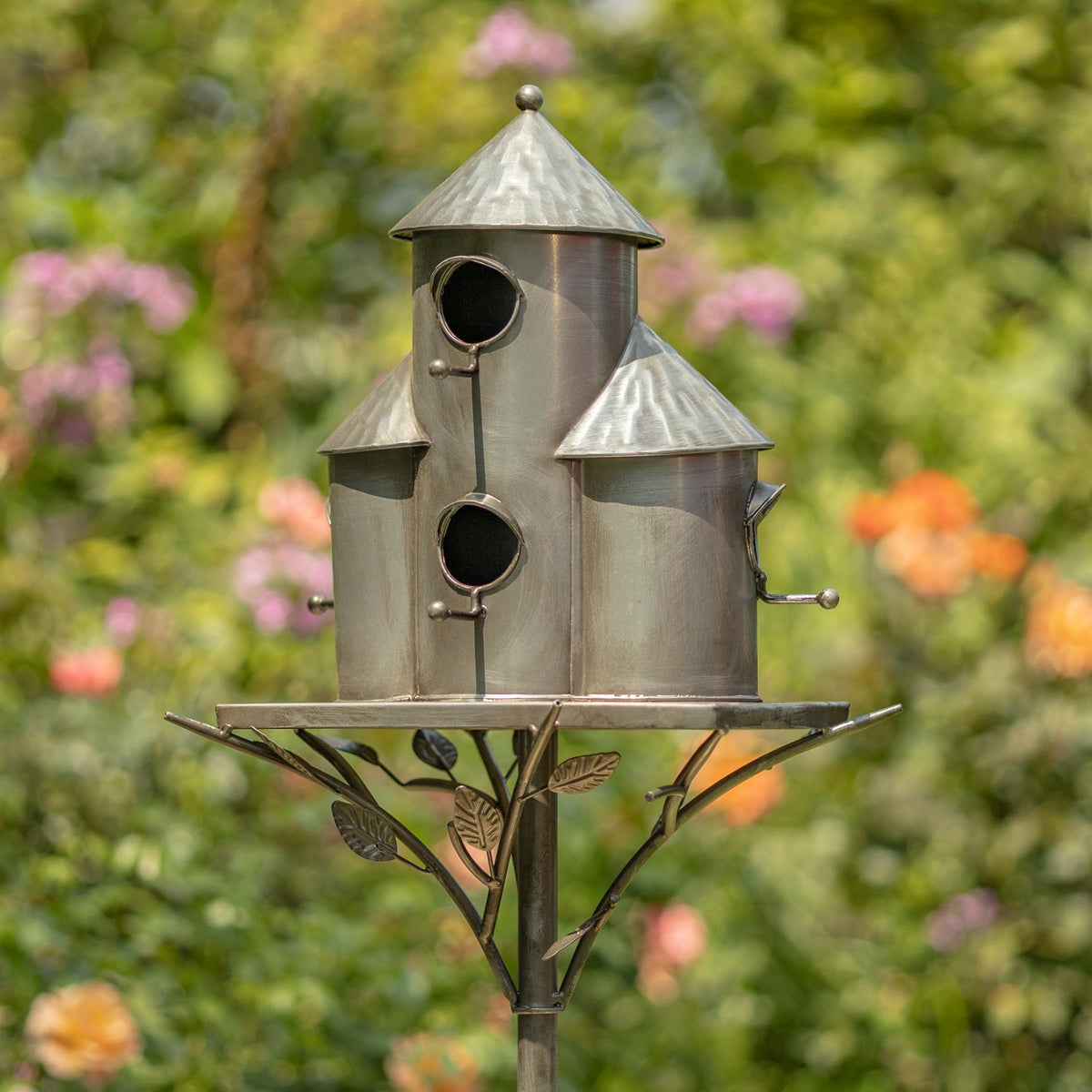 Three silver birdhouses at different heights on a round platform above branching decorative metal leaves.