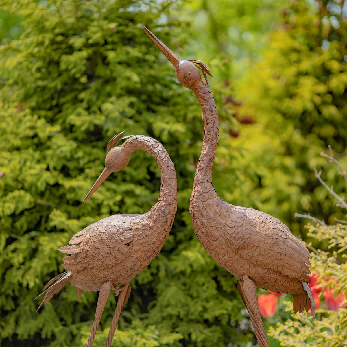 Closer view of two textured rust-finish crane sculptures against greenery