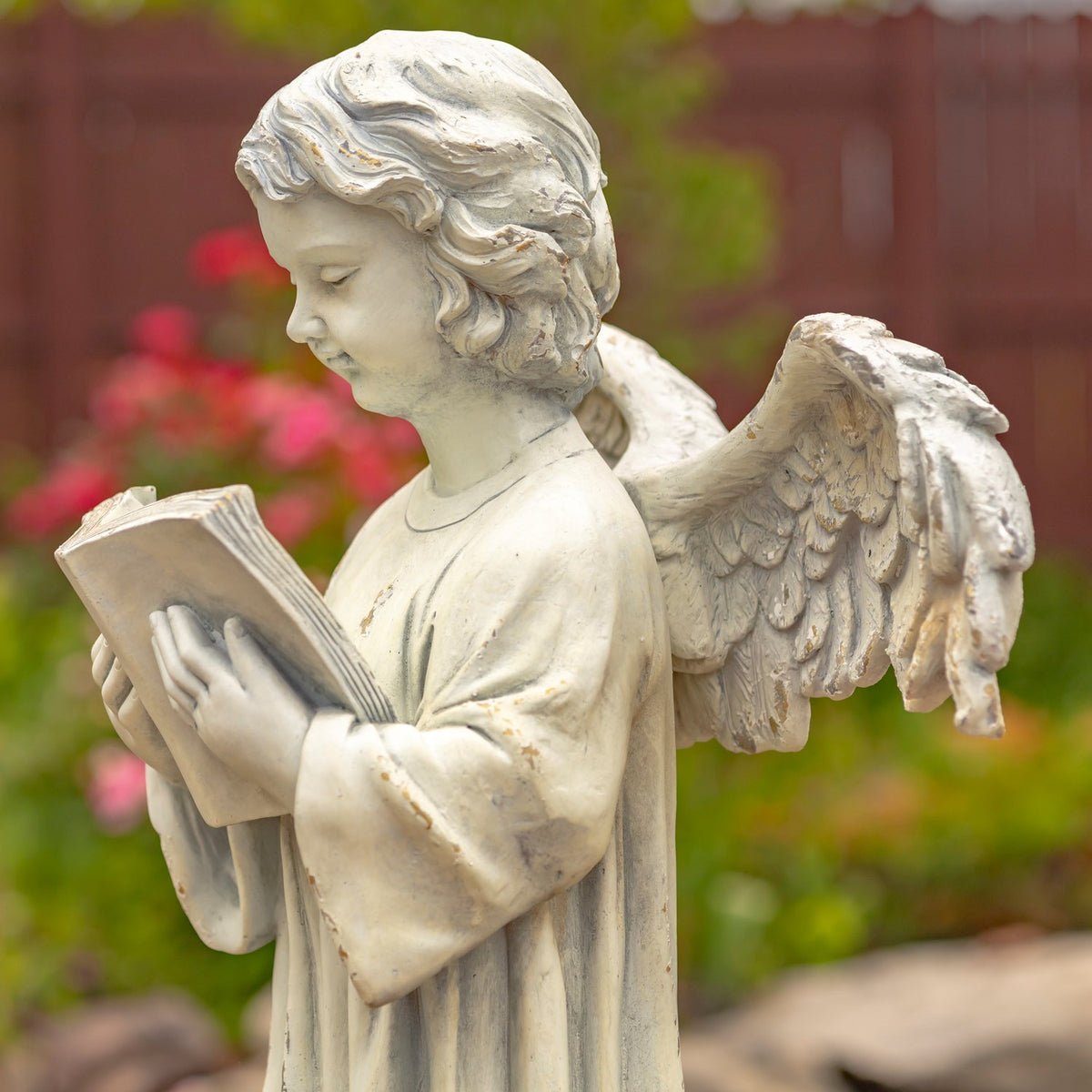 Side view showing the angel’s carved hair, open book, robe, and layered wing feathers.