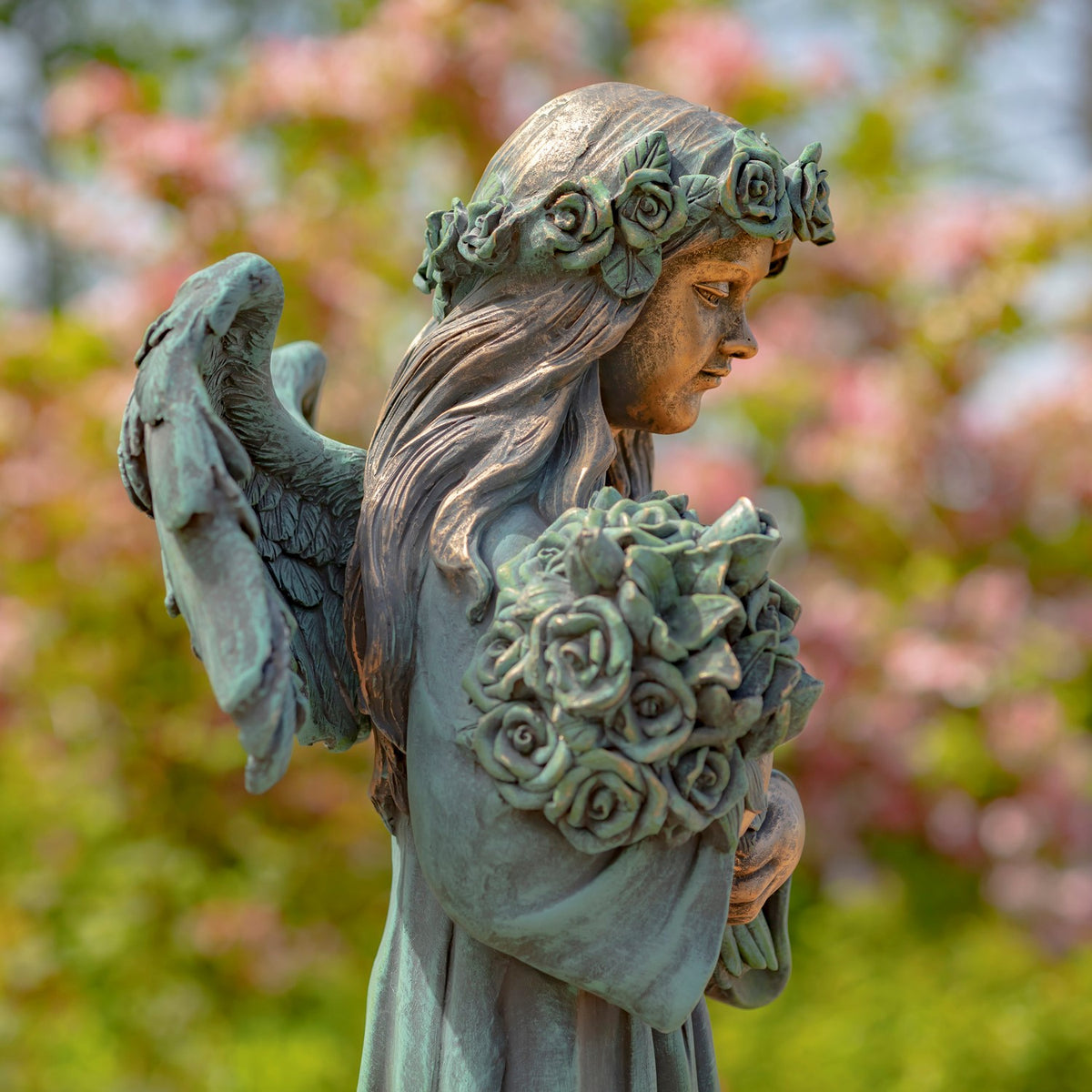 Side view shows the statue’s wing, rose crown, flowing hair, and bouquet held close to her chest.